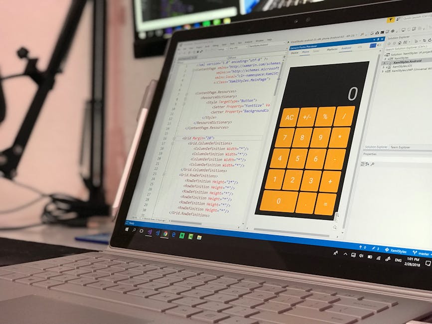 A close-up view of a laptop with an open screen displaying lines of code in a text editor alongside a digital calculator app with orange buttons showing basic arithmetic functions. The laptop is place